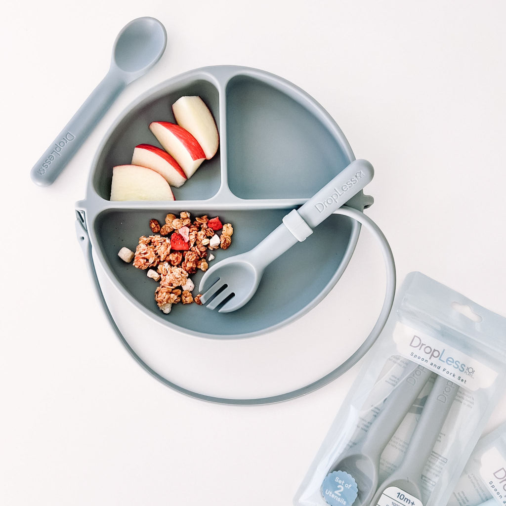 Children's plate with compartments, fork, spoon, and snacks on a white background
