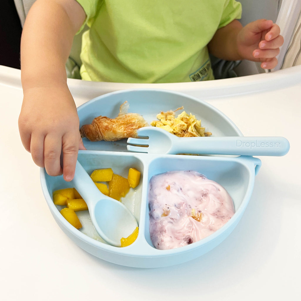 Child using a blue divided plate with utensils on a white table